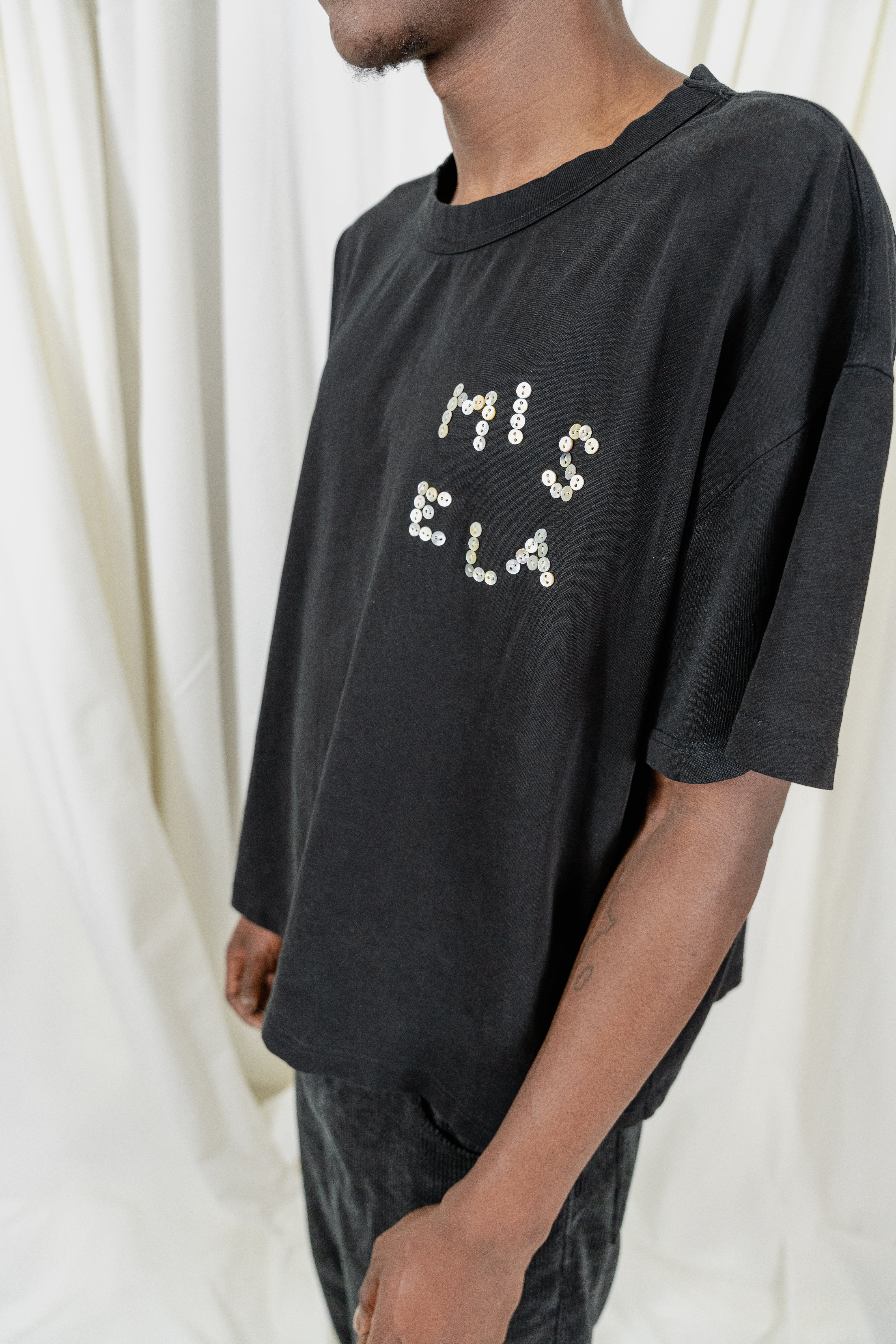 Model Fullsize wearing Signature Peral Tee in Black from Misela Studios in front of a cloth screen - Frontview Detail