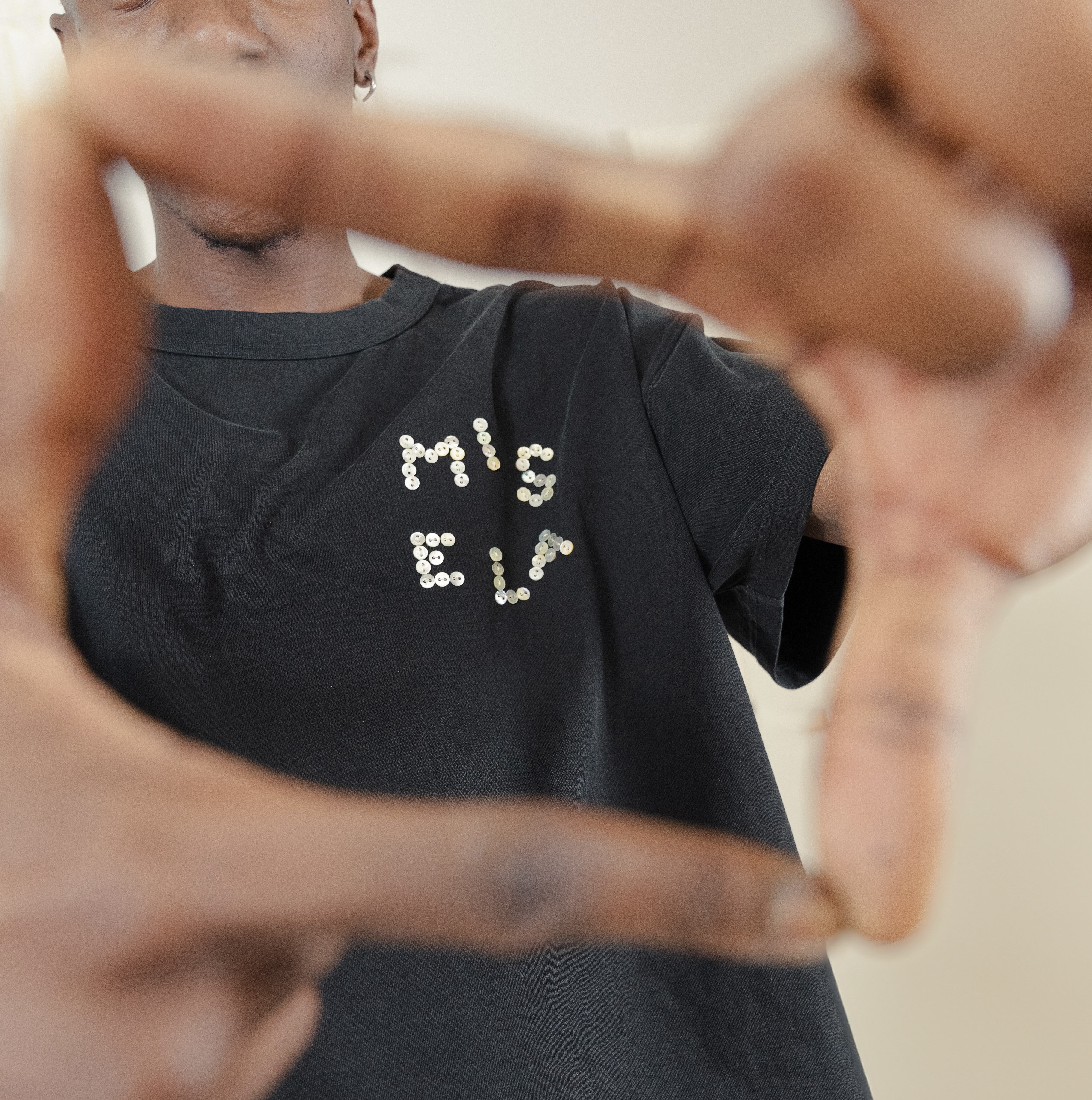 Model wearing Signature Pearl Tee and focusing on the Misela Studios Logo Embroidery