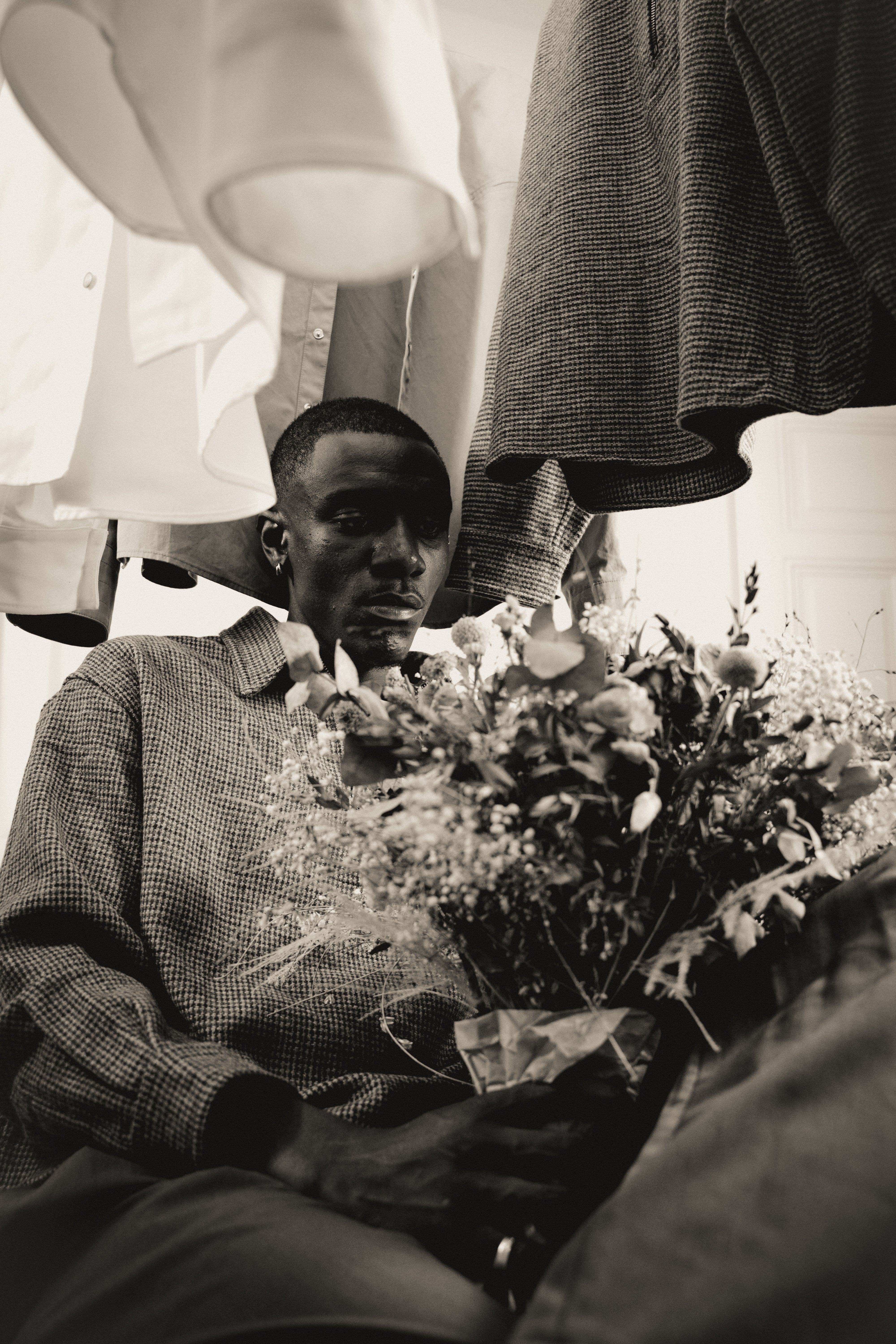 Model is sitting with dry flowers in hand in front of hanging cloths from misela studios