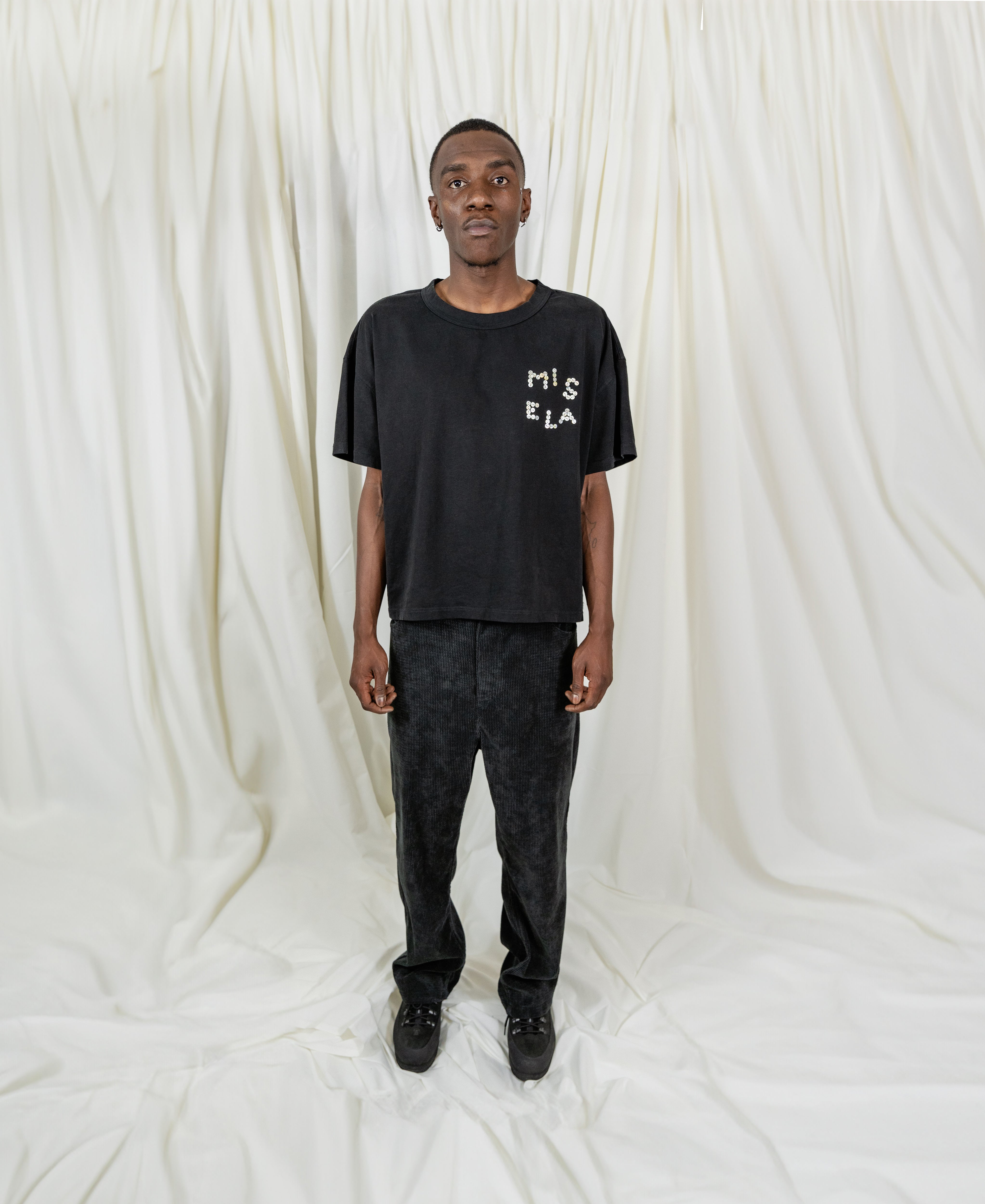 Model Fullsize wearing Signature Peral Tee in Black from Misela Studios in front of a cloth screen - Frontview
